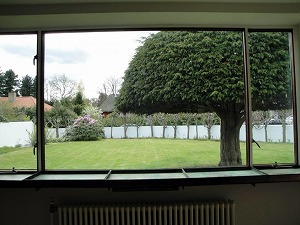 居間から庭を見た風景。窓の脇に銅板製の観賞植物の鉢を置く箱がある。