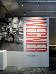 ウェグナ—が自分の椅子に座る写真パネルがある、展覧会入口。