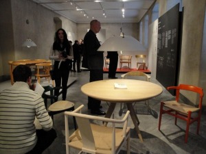 展覧会会場では、見学者は色々な椅子に座って居心地を楽しめる。天井から下がっているランプもウェグナ—のデザイン。