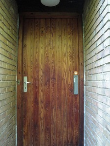 正面玄関の塗料がぬられていない、木目が浮き上がったオリジナルのドア。残念ながら、古いドアは防犯に弱いので、新しいドア金具にするように奨励されている。